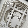 Paper cutout depicting a spooky Halloween scene with a pumpkin-headed scarecrow, bats, and carved pumpkins in front of a window.