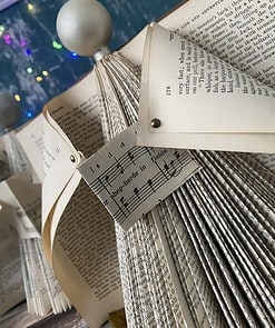 Folded book pages create a Christmas tree shape with sheet music and colorful lights in the background.