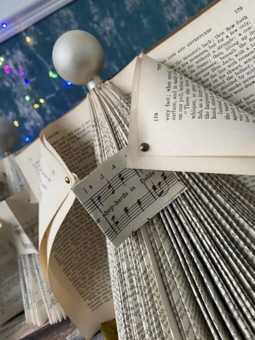 Folded book pages create a Christmas tree shape with sheet music and colorful lights in the background.