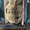 Book pages folded to form the shape of an apple with the words "teacher life" and a heart carved into them, placed on two other books.