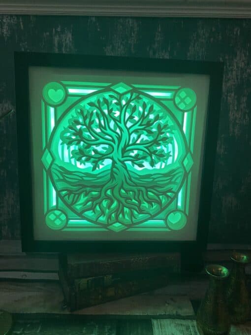 Glowing green framed artwork depicting a tree with roots, illuminated against a textured dark wall.