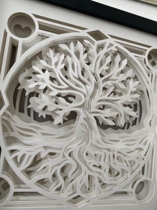 Intricate white paper cut-out depicting a stylized tree with roots, framed in geometric shapes.