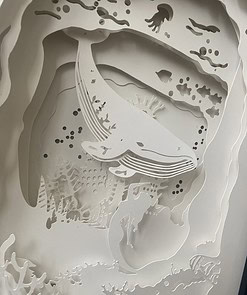 Intricate paper art depicting an underwater scene with a whale, fish, coral, and a mermaid silhouette.