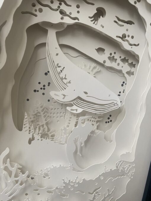 Intricate paper art depicting an underwater scene with a whale, fish, coral, and a mermaid silhouette.