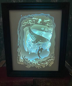 Framed illuminated artwork of an underwater scene with a whale, mermaid, coral, and jellyfish, glowing in blue tones.