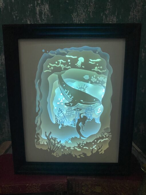 Framed illuminated artwork of an underwater scene with a whale, mermaid, coral, and jellyfish, glowing in blue tones.