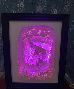 Framed luminous sea scene with a whale and coral, glowing in purple and pink hues against a dark background.