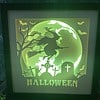 Illuminated Halloween display showing a witch on a broomstick, a graveyard with tombstones, bats, and "HALLOWEEN" text.