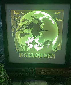 Illuminated Halloween display showing a witch on a broomstick, a graveyard with tombstones, bats, and "HALLOWEEN" text.