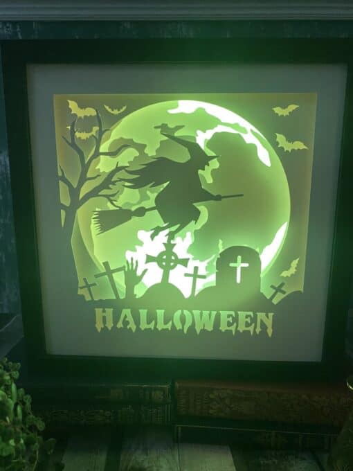 Illuminated Halloween display showing a witch on a broomstick, a graveyard with tombstones, bats, and "HALLOWEEN" text.