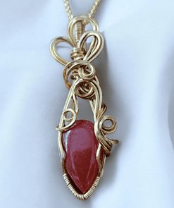 Gold pendant with intricate wire design enclosing a reddish gemstone, hanging from a twisted gold chain, on a white background.