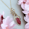 Gold necklace with a red gemstone pendant surrounded by pink flowers.