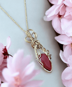 Gold necklace with a red gemstone pendant surrounded by pink flowers.