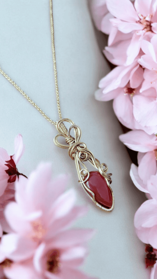 Gold necklace with a red gemstone pendant surrounded by pink flowers.