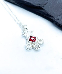 Silver necklace pendant with a star shape, featuring a central red gem and two smaller clear crystals, displayed on a white background.