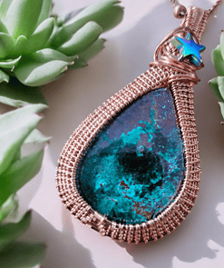 Close-up of a handcrafted teardrop pendant with a blue-green stone set in intricate wire wrapping, surrounded by succulents.