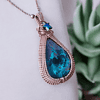 Close-up of a teardrop-shaped pendant with a blue-green stone and woven metal frame, accented with a small blue star charm.