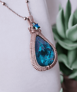 Close-up of a teardrop-shaped pendant with a blue-green stone and woven metal frame, accented with a small blue star charm.