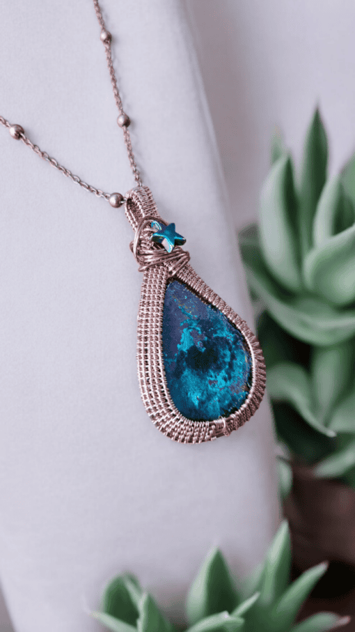 Close-up of a teardrop-shaped pendant with a blue-green stone and woven metal frame, accented with a small blue star charm.