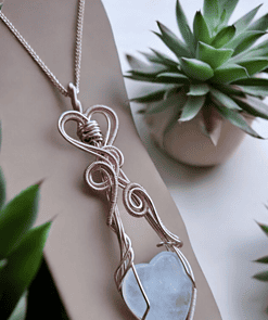 Silver wire-wrapped heart pendant with gemstone jewellery charms displayed among succulent plants.