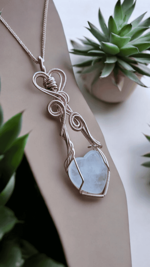 Silver wire-wrapped heart pendant with gemstone jewellery charms displayed among succulent plants.