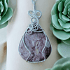 Silver wire-wrapped pendant with a purple stone on a chain, surrounded by green succulents in the background.