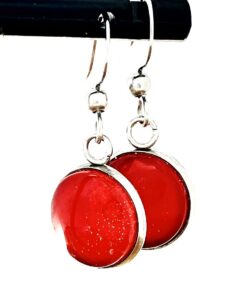 Silver hoop earrings with round red glass pendants, hanging from a black rod.