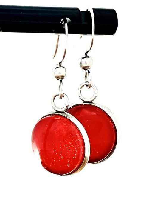 Silver hoop earrings with round red glass pendants, hanging from a black rod.