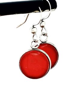 Two red circular earrings with silver edges and hooks, hanging on a black rod.