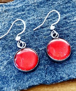 Red round glass earrings with silver hooks on a textured blue surface.