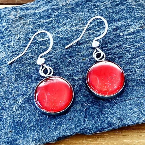 Red round glass earrings with silver hooks on a textured blue surface.