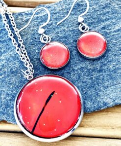 Red resin pendant and earrings with silver tone settings on a textured rock background.