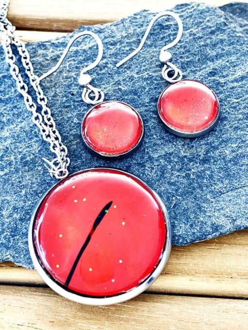 Red resin pendant and earrings with silver tone settings on a textured rock background.