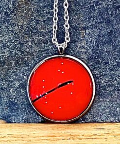 Red circular pendant with a black line and small white dots, hanging on a silver chain against a textured dark background.