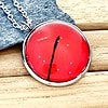 Red pendant with black line detail on silver chain, placed on gray stone, wooden background.