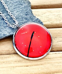 Red pendant with black line detail on silver chain, placed on gray stone, wooden background.