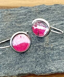 Silver cufflinks with pink and white enamel accents on a textured slate surface.