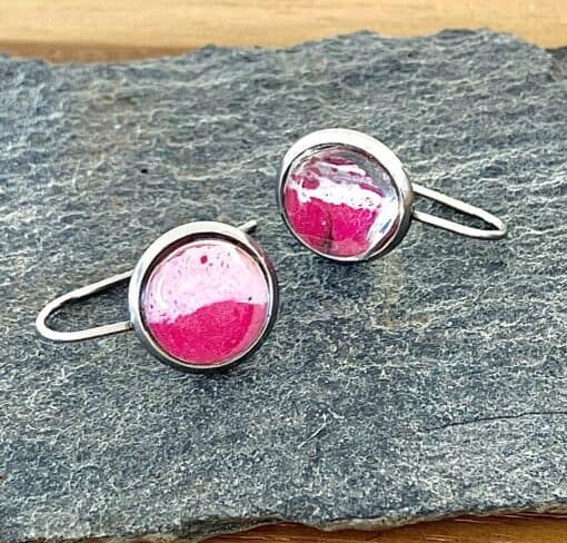 Silver cufflinks with pink and white enamel accents on a textured slate surface.