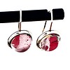 Two round earrings with pink and white marbled stones set in silver hooks, hanging on a black rod.