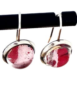 Two round earrings with pink and white marbled stones set in silver hooks, hanging on a black rod.