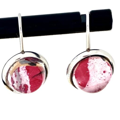 Round pink and white gemstone earrings with silver frames, hanging on a horizontal black rod.