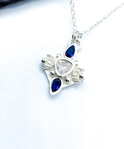 Silver star-shaped pendant with a central clear gem, accented by blue teardrop-shaped stones on a delicate silver chain.