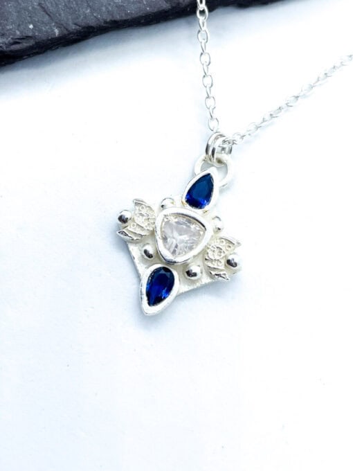 Silver star-shaped pendant with a central clear gem, accented by blue teardrop-shaped stones on a delicate silver chain.