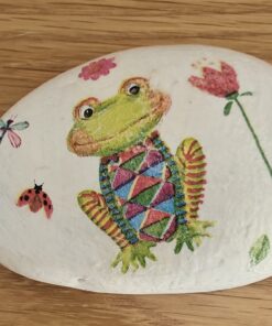 A hand-painted rock featuring a colorful frog, a dragonfly, a ladybug, and flowers on a wooden surface.