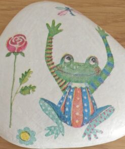 Painted rock with a colorful frog wearing striped clothes, a rose, and a dragonfly, placed on a wooden surface.