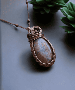 Handmade wire wrapped necklace with a large stone pendant, set on a chain, displayed beside green succulents.