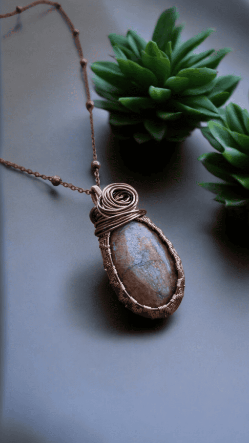 Handmade wire wrapped necklace with a large stone pendant, set on a chain, displayed beside green succulents.