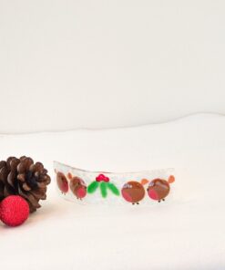 Festive hair clip with red and green reindeer design, surrounded by pinecones and a red glitter bauble on white background.