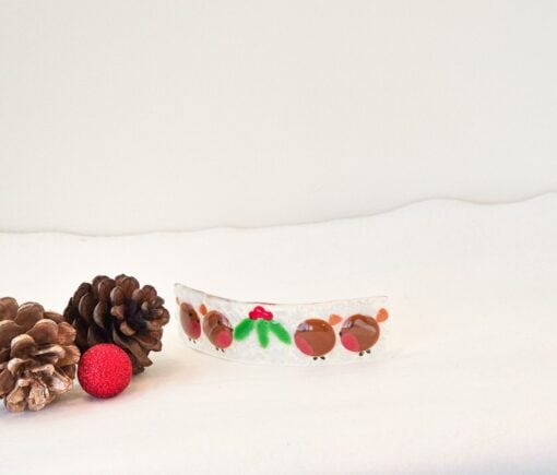 Festive hair clip with red and green reindeer design, surrounded by pinecones and a red glitter bauble on white background.