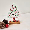 Glass Christmas tree with red, green, and white decorations on a wooden base, surrounded by pinecones and a red ornament.